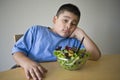 Unhappy preadolescent Boy Sitting At Desk With Salad