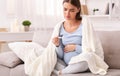 Unhappy pregnant lady having fever feeling bad sitting on sofa