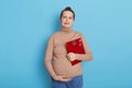 Unhappy pregnant woman holding scales on blue background, being sad, frowning face, suffers from gaining excess weight,