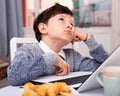 Unhappy preteen boy sitting near laptop at home table