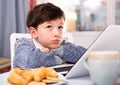 Unhappy preteen boy sitting near laptop at home table