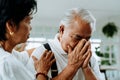 Unhappy retired Asian senior couple sitting on the sofa while elderly wife comforting her sad husband at home.