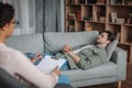 Unhappy sad european male patient lies on sofa, listens to black female psychologist in office clinic interior