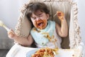 Unhappy sad toddler child messy tomato sauce on mouth crying. Upset messy little girl hungry eating spaghetti with spaghetti spoon