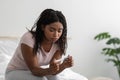 Unhappy sad young african american woman with pregnancy test sit on bed in white bedroom interior Royalty Free Stock Photo