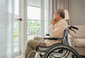 Unhappy senior retirement Asian man sitting alone in a wheelchair and looking outside window from depression and loneliness in Royalty Free Stock Photo