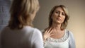 Unhappy senior woman looking in mirror and touching decollete zone, wrinkles