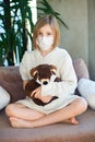 Unhappy sick toddler girl wearing medicine mask for protection sitting with toy teddy bear