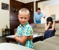 Unhappy small boy sitting at sofa during his parents quarrelling