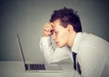 Unhappy stressed sad man sitting at desk in front of his laptop