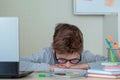 Unhappy and strssed school boy studying with a notebooks on his desk at home. Child is tired of online learning. Kid rests face Royalty Free Stock Photo