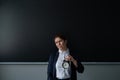 Unhappy teacher in a pantsuit holding an alarm clock while standing at the blackboard. Royalty Free Stock Photo