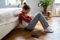 Unhappy teen girl covering face with hands crying while sitting on floor with mobile phone nearby Royalty Free Stock Photo