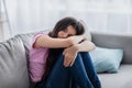 Unhappy teen girl feeling depressed or desperate, sitting on couch at home, suffering from problem or teenage depression