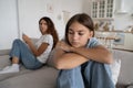 Offended teen girl feeling sad after argument with parent, sitting separately with mother on sofa