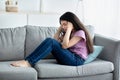 Unhappy teen girl holding her head in despair, feeling depressed, sitting on sofa at home, copy space