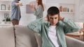 Unhappy teenage boy covering ears while his parents arguing on background. Problems at home Royalty Free Stock Photo