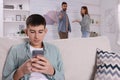 Unhappy teenage boy scrolling through phone while his parents arguing on background. Problems at home Royalty Free Stock Photo
