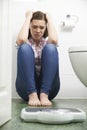Unhappy Teenage Girl Sitting On Floor Looking At Bathroom Scales Royalty Free Stock Photo