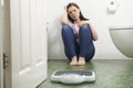 Unhappy Teenage Girl Sitting On Floor Looking At Bathroom Scales Royalty Free Stock Photo