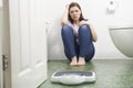 Unhappy Teenage Girl Sitting On Floor Looking At Bathroom Scales Royalty Free Stock Photo