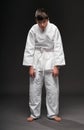 Unhappy teenager dressed in martial arts clothing poses on a dark gray background, having depression, sports concept