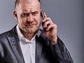 Unhappy tired angry business man talking on mobile phone and holding in hand one more phone in office suit on grey studio Royalty Free Stock Photo