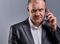 Unhappy tired angry business man talking on mobile phone and holding in hand one more phone in office suit on grey studio Royalty Free Stock Photo