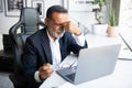 Unhappy tired european senior businessman in suit resting at table with computer in office Royalty Free Stock Photo