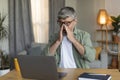 Unhappy tired retired caucasian male in glasses rubs his eyes, sitting at table, working with computer Royalty Free Stock Photo
