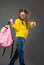 Unhappy tired schoolgirl in eyeglasses holding the pink backpack on grey studio background in fashion style clothing and showing