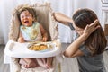 Unhappy toddler child with tomato sauce on her face crying with her mother sitting together beside in the room. Upset messy little Royalty Free Stock Photo