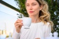 Unhappy woman drinking a cup of coffee. Outdoor terrace lunch. White dresses Royalty Free Stock Photo