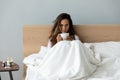 Unhappy woman feeling holding cup of tea, sitting in bed Royalty Free Stock Photo