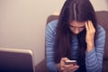 Unhappy woman with headache sitting near the laptop and writing sms in mobile phone. Closeup portrait of business person on work Royalty Free Stock Photo