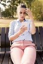 Unhappy woman sitting on bench in autumn park with mobile phone Royalty Free Stock Photo