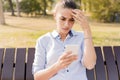 Unhappy woman sitting on bench in autumn park with mobile phone Royalty Free Stock Photo