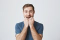 Unhappy worried sad man with beard in blue t-shirt clenches teeth, bites nails, is afraid of hearing bad news, has