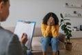 Unhappy young African American woman covering face with hands, crying on session with psychologist at office Royalty Free Stock Photo