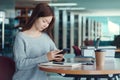 Unhappy young asian woman talking on mobile phone while reading book in library Royalty Free Stock Photo