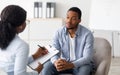 Unhappy young black man having session with professional psychologist at mental health clinic Royalty Free Stock Photo