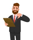 Unhappy young businessman wearing a suit holding clipboard and making or showing thumbs down gesture or sign. Person keeping file. Royalty Free Stock Photo