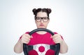 Unhappy young girl in glasses with steering wheel, on light background. Front view. Female car driver concept Royalty Free Stock Photo