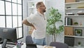 Unhappy young man worker suffering from backache while standing indoors at the office, serious business professional touching Royalty Free Stock Photo