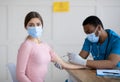 Unhappy young woman in face mask feeling afraid of pain during covid-19 vaccine shot at medical office Royalty Free Stock Photo