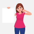 Unhappy young woman holding a blank / empty sheet of white paper or board and gesturing thumbs down sign.