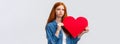 Unhapy brokenhearted cute redhead girl, sulking and looking up uneasy, distressed holding big red valentines day heart Royalty Free Stock Photo