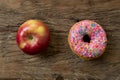 Unhealthy but delicious sweet sugar donut cake versus healthy apple fruit on vintage wooden table in lifestyle nutrition