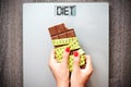 Unhealthy diet concept with woman hand holding chocolate bar on weighting scale with rolled measurement tape