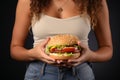 Unhealthy eating concept Womans connection to greasy burger, hand on stomach, gray background